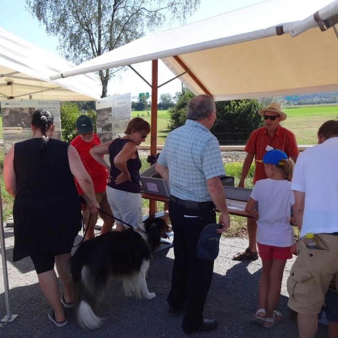 Besucherinnen und Besucher am Infostand beim UNESCO-Welterbetag, Archäologe erklärt Funde