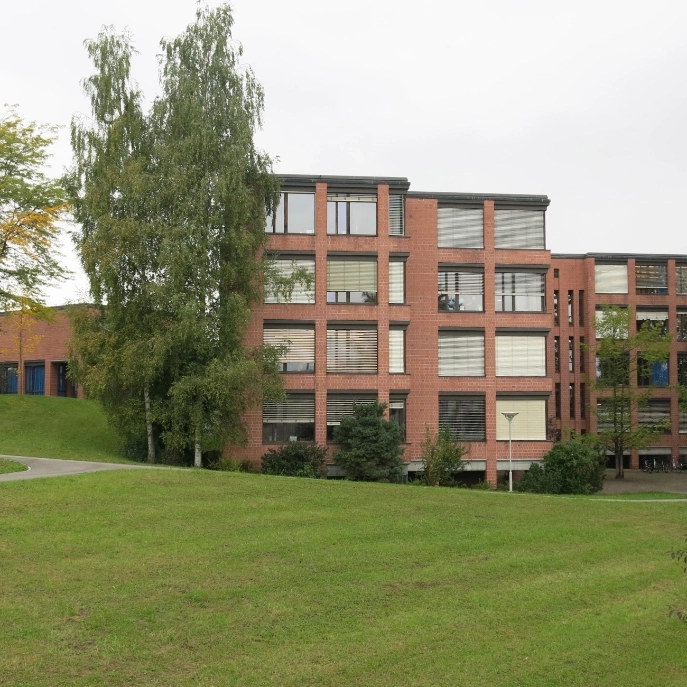 Ansicht einer Fassade des Schulhauses Röhrliberg mit einer Wiese und Bäumen im Vordergrund