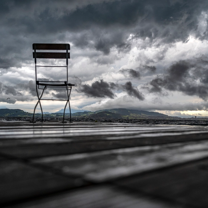 Ein Gartenstuhl steht auf dem Holzdeck des Seebad Seelikon in Zug, im Hintergrund der aufziehende Gewittersturm vom 28. Juni 2021 mit bedrohlichen Wolken
