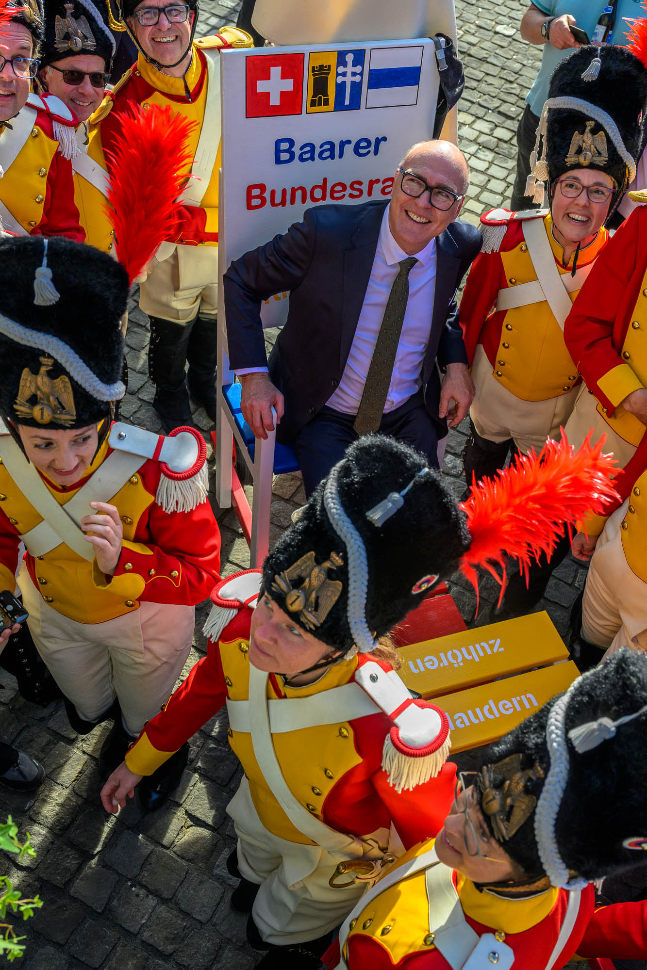 Bundesrat Martin Pfister sitzt auf den Baarer Bundesratsstuhl. Er wird von Beresina Grenadieren in Uniform umringt.