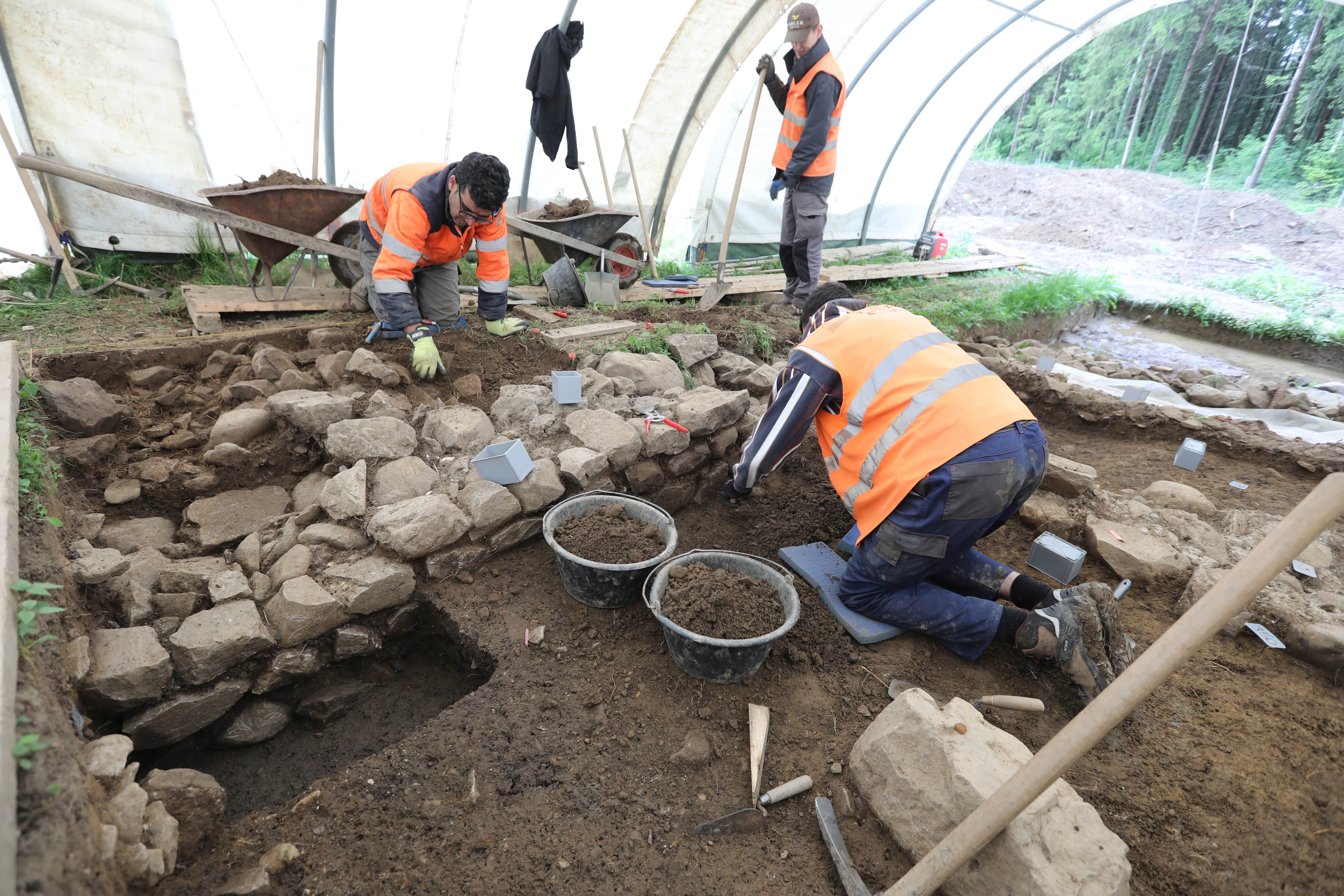 Ausgräber im Zelt kniend, beim Ausgraben der römischen Mauer